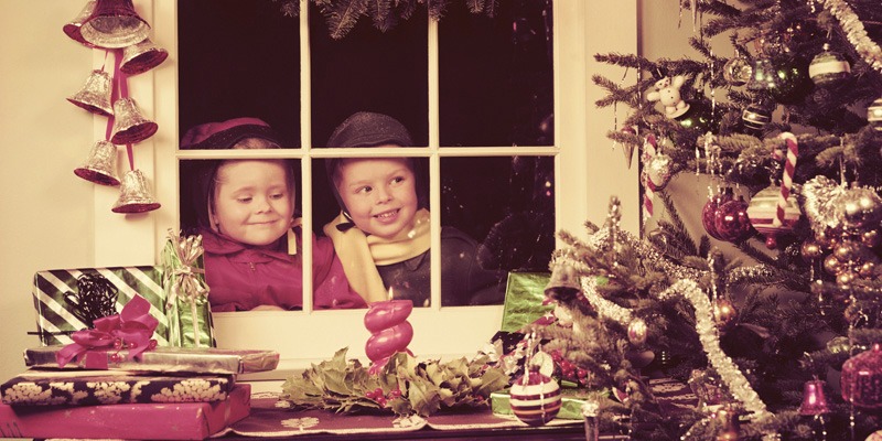 Two kids standing outside looking into a window at a Christmas tree