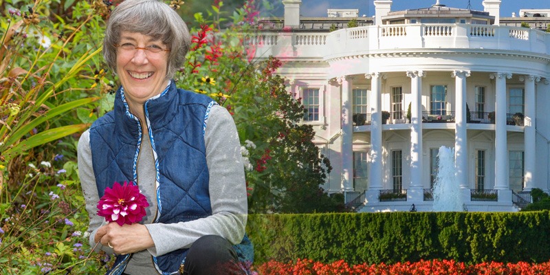 Marta McDowell squatting and holding a flower in front of the White House